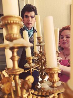 a man standing next to a woman in front of a chandelier with candles