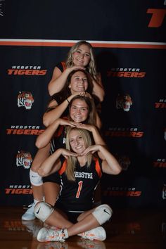 a group of young women sitting on top of each other in front of a wall