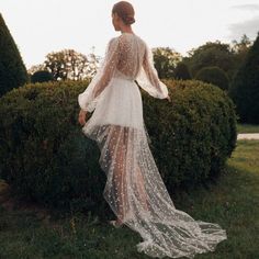 a woman standing in front of a bush wearing a white dress with pearls on it