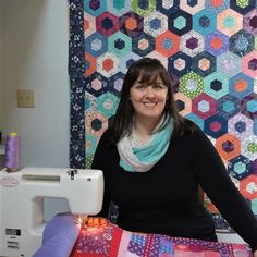 a woman standing in front of a quilting machine and smiling at the camera,