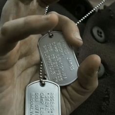 a person holding two dog tags in their hands, one is silver and the other is black