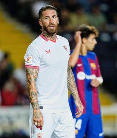 a man with tattoos on his face standing next to another man in a soccer field