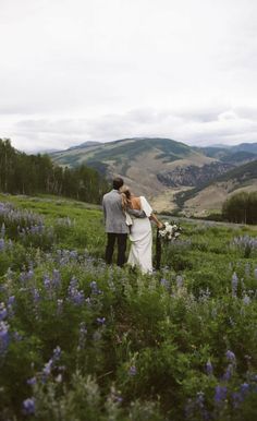 a bride and groom standing in the middle of a field with mountains in the background