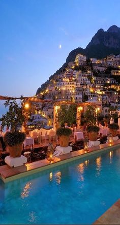 an outdoor swimming pool with lounge chairs and umbrellas next to the water at night