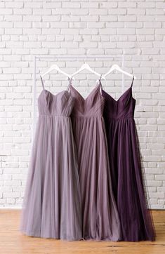 three bridesmaid dresses hanging up against a brick wall