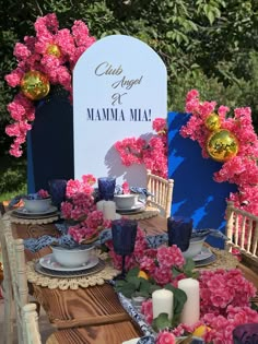 the table is set with pink flowers and blue chinaware for an outdoor tea party