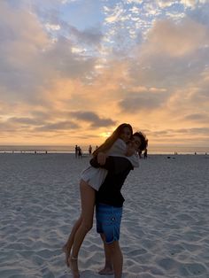 two people hugging each other on the beach at sunset with clouds in the sky behind them