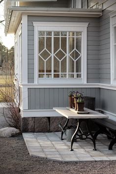 a table and bench in front of a gray house with white trim on the windows