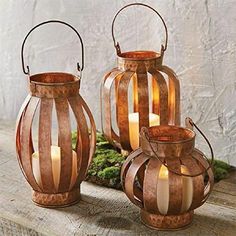 three metal lanterns with candles in them sitting on a wooden table next to moss and rocks