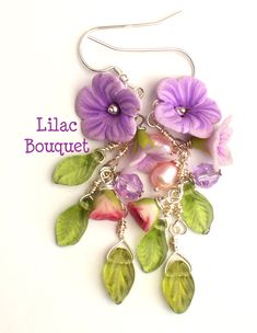 purple flowers and green leaves are hanging from silver earwires on a white background