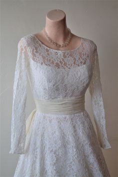 a white dress on a mannequin with a belt around the waist and long sleeves