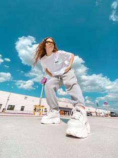 a woman in white shirt and grey sweatpants standing on top of a skateboard