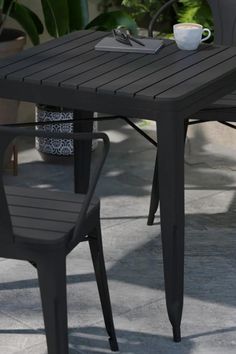 an outdoor table with two chairs and a coffee cup on it next to potted plants