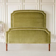 an upholstered bed frame with wooden legs and headboard in a white room