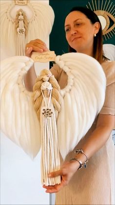 a woman holding an angel statue with white wings and tassels on it's back