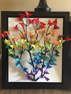 an origami tree made out of folded paper in a black frame on a wooden floor