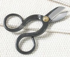 a pair of black scissors sitting on top of a piece of white fabric with gold buttons