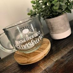 a glass mug sitting on top of a wooden stand next to a potted plant