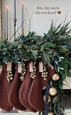 stockings hanging from a mantel decorated with greenery and candles