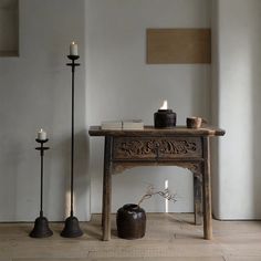 an old table with candles on it next to two black candle holders and a vase