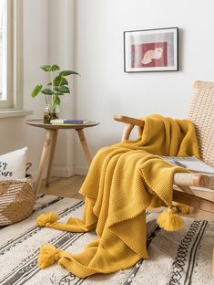 a yellow blanket is draped over a wooden chair in a white room with potted plants