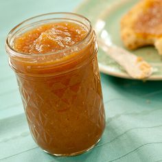 a glass jar filled with jam sitting on top of a table next to a piece of bread