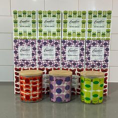 four candles are lined up in front of each other on a counter top with colorful wrapping paper behind them