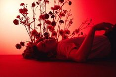 a woman laying on the floor with flowers in front of her and red light behind her