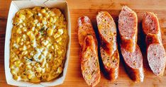 some sausages and corn in a box next to other food on a wooden table