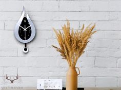 a clock on the wall above a vase with dry grass