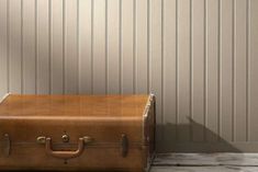 a brown suitcase sitting on the floor in front of a wall with vertical striped paneling