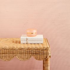 a wicker table with a candle and some books on it next to a pink wall