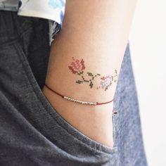 a woman's arm with a cross stitch bracelet on it and a rose tattoo