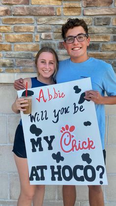 two people holding up a sign that says abbie will you be my chick at hoco?