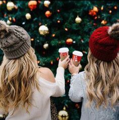 two women standing next to each other in front of a christmas tree holding coffee cups