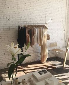 a white brick wall with clothes hanging on racks and two vases filled with flowers