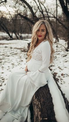 a woman sitting on top of a tree stump in the snow wearing a white dress