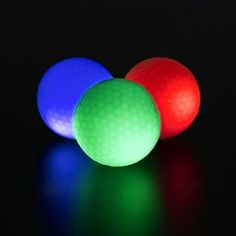 three different colored golf balls sitting next to each other on a black surface with one red, one blue and one green