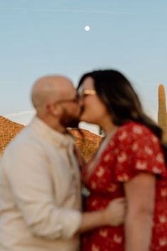 a man and woman kissing each other in front of a saguada with the moon behind them