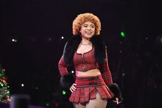 a woman in a red and black outfit on stage with a christmas tree behind her