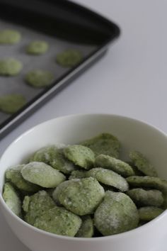 a white bowl filled with green cookies on top of a counter next to a cookie sheet