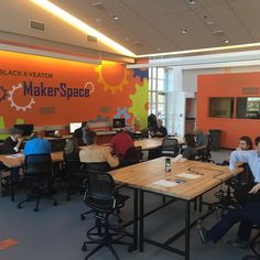 people sitting at desks working on laptops in an open office space with orange walls