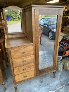 a large wooden dresser sitting next to a car in a garage with a mirror on it's side