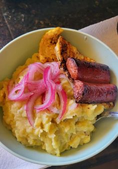 a white bowl filled with mashed potatoes and sausage on top of it next to a cup of coffee