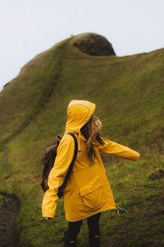 a woman in a yellow raincoat walking up a hill with her back to the camera