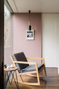 a modern rocking chair in the corner of a room with pink walls and wood flooring