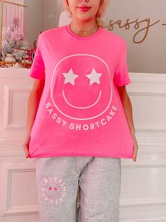 We are so excited to release our newest merch item! The Sassy Star Pink Smiley Tee is a hot pink t-shirt with a white smiley face with star eyes. She also features the text "Sassy Shortcake" in white. Rep your favorite brand in this super cute tee!! Oversized fit + unisex sizing. Model is wearing a size small. Sparkle Romper, Sassy Shortcake, Pink Smiley, Patriotic Dresses, Preppy Girls, Pink Iridescent, Star Eyes, Aesthetic Outfit Ideas, Casual Preppy Outfits