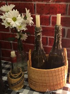 three bottles in a basket on a table next to flowers and a vase with two candles