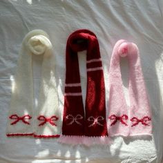 three knitted scarves laid out on top of a white sheet with red and pink designs