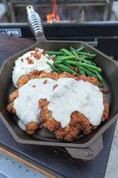 a skillet filled with fried chicken, mashed potatoes and green beans on top of a table